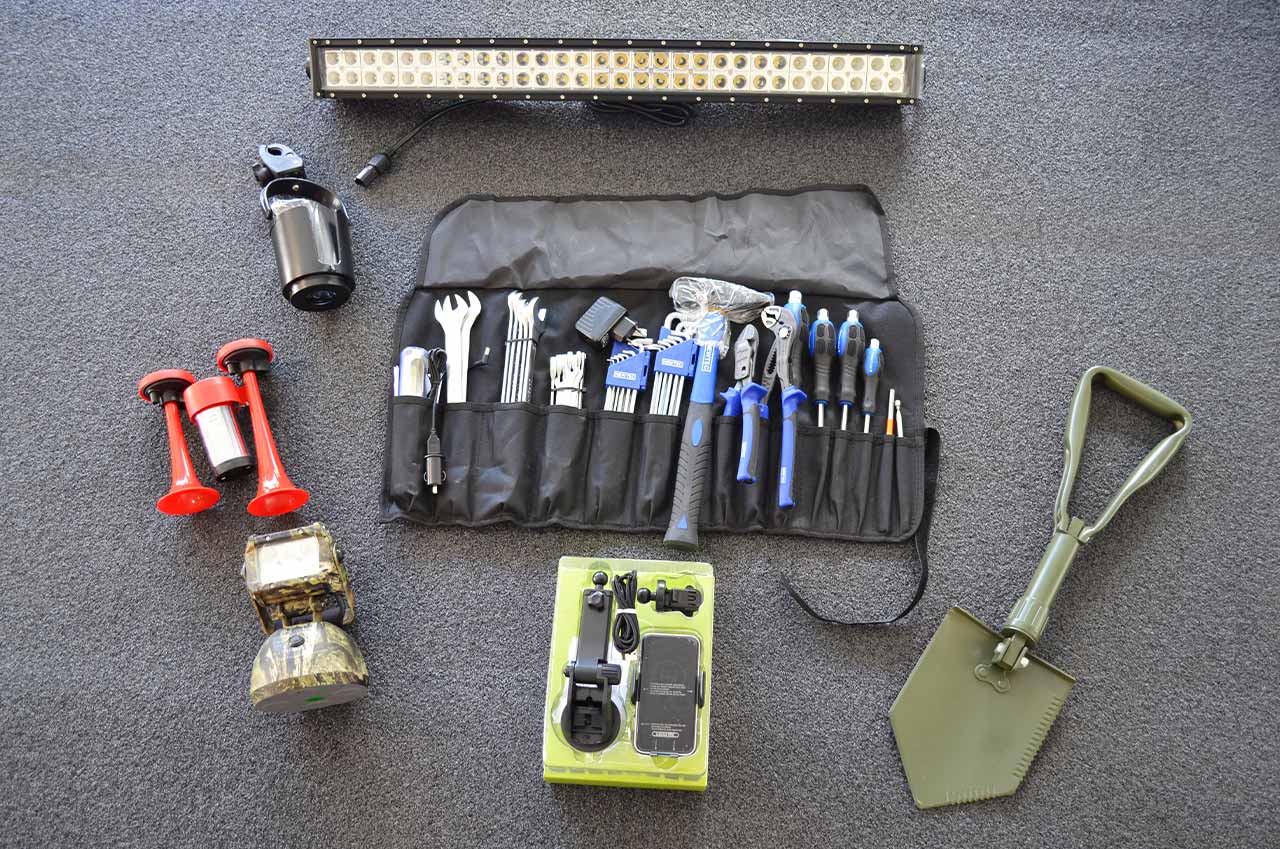 Werkzeugset mit Hammer, Schraubenschlüsseln, Schraubenziehern und Zangen in einer schwarzen Rolltasche, Klappspaten, Handyhalter, LED-Akku-Scheinwerfer, Drucklufthupe, Getränkehalter und LED-Lichtleiste